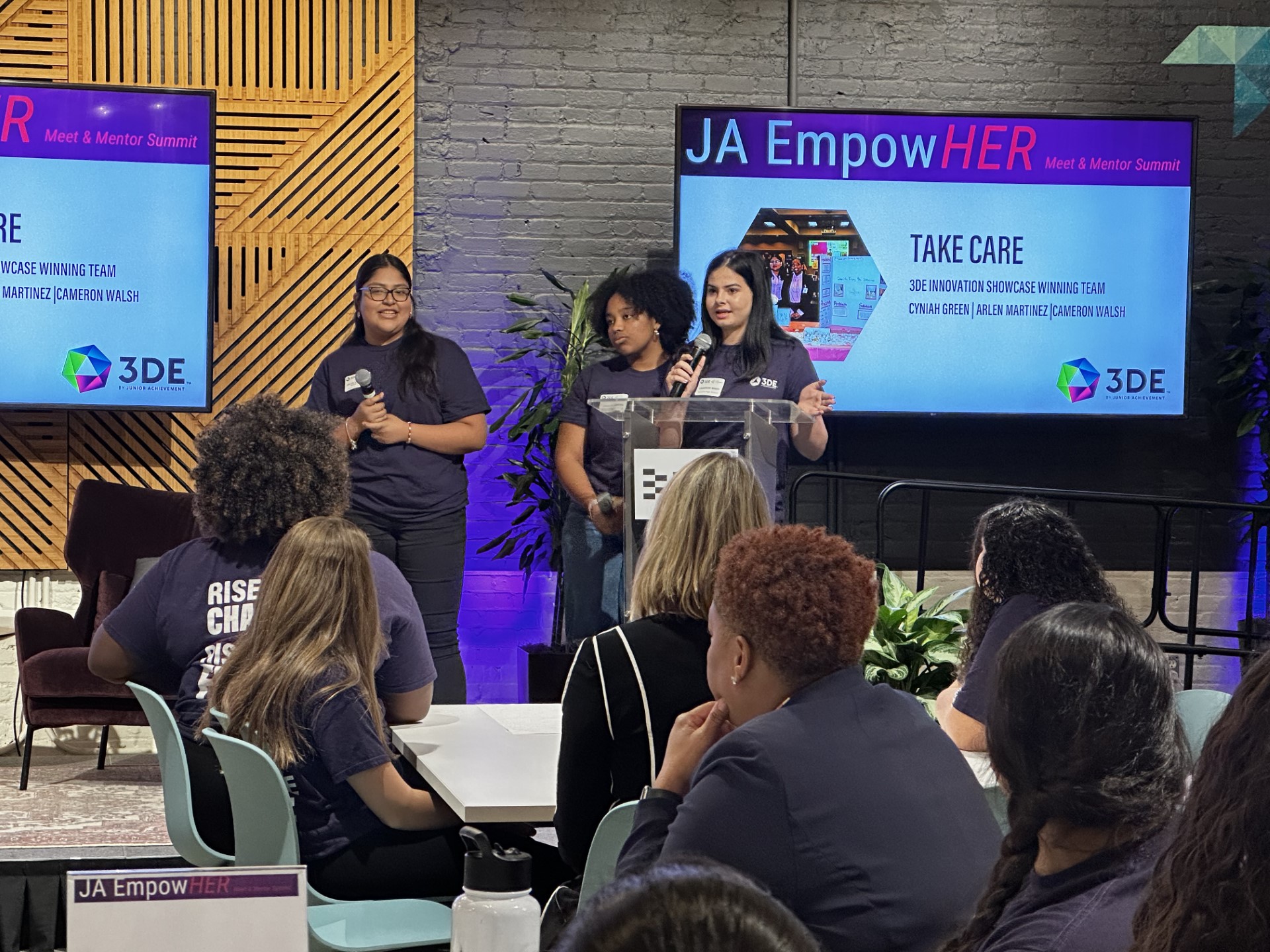 A group of women standing in front of a large screenDescription automatically generated